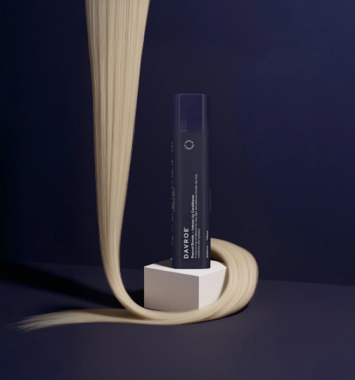 Hair product bottle on a stand with blonde hair strands against a dark background