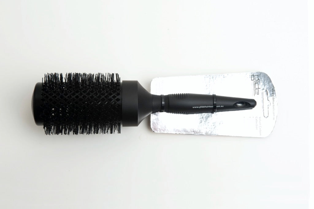 A black jumbo brush with a carbon-coated surface, displayed on a white background, packaged with a label.