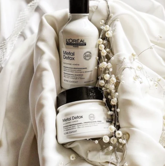 L'Oreal Metal Detox shampoo and mask set on a soft fabric background with decorative elements.